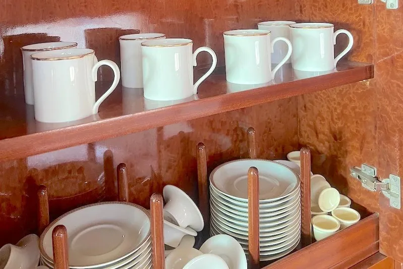 Curiosity Yacht Photos Pics White ceramic mugs and plates neatly arranged in a wooden cabinet.