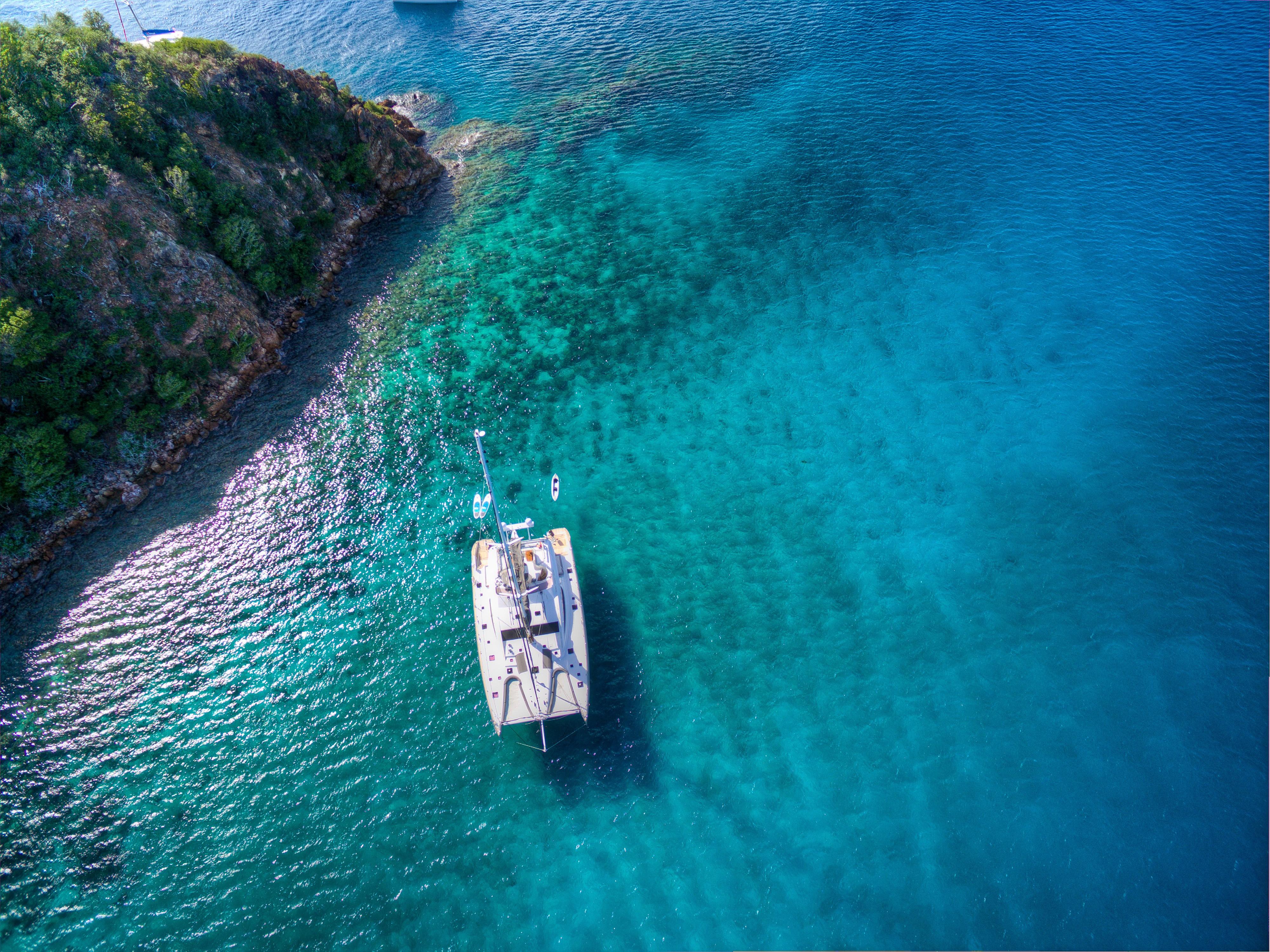 Aerial view of a 2010 Privilege 745 yacht anchored near a rocky coastline in clear blue water.