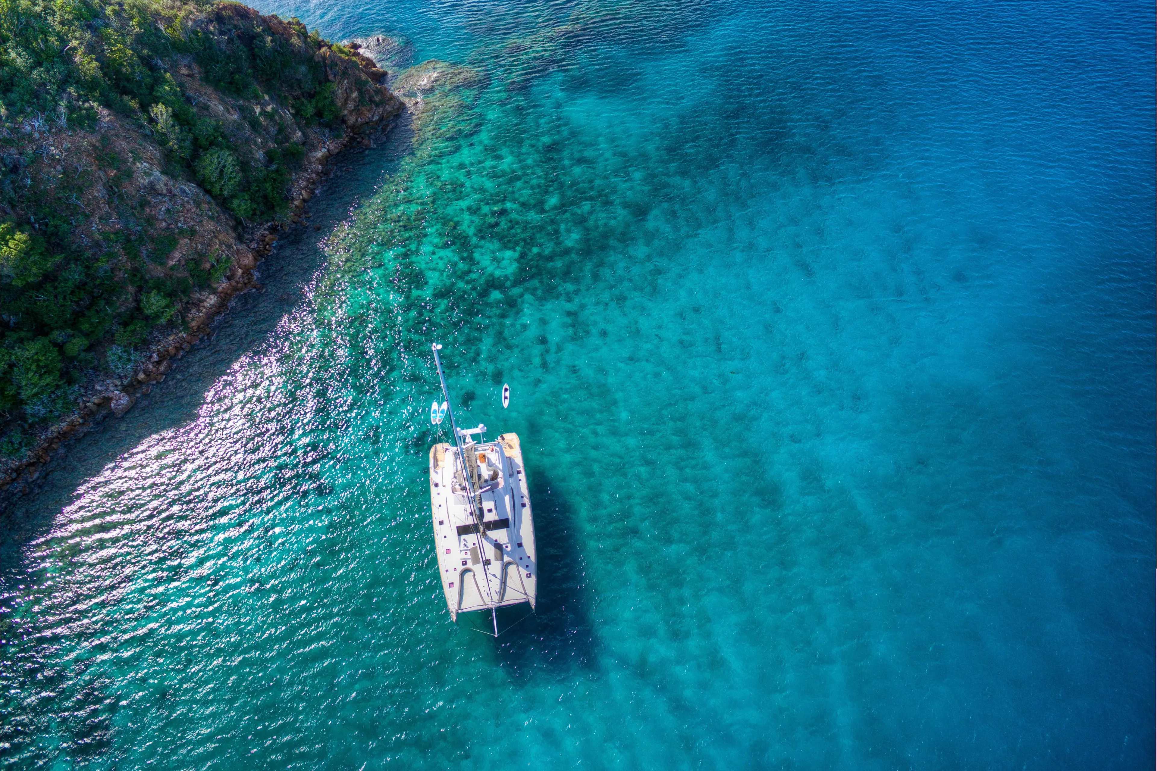 Aerial view of a 2010 Privilege 745 yacht anchored near a rocky coastline in clear blue water.