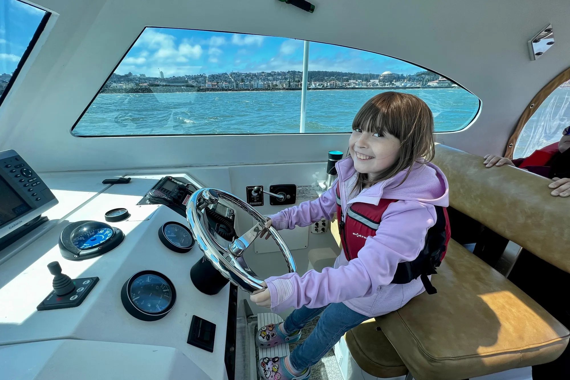 Young girl steering a 1999 Mainship Pilot 30 boat, smiling on a sunny day.