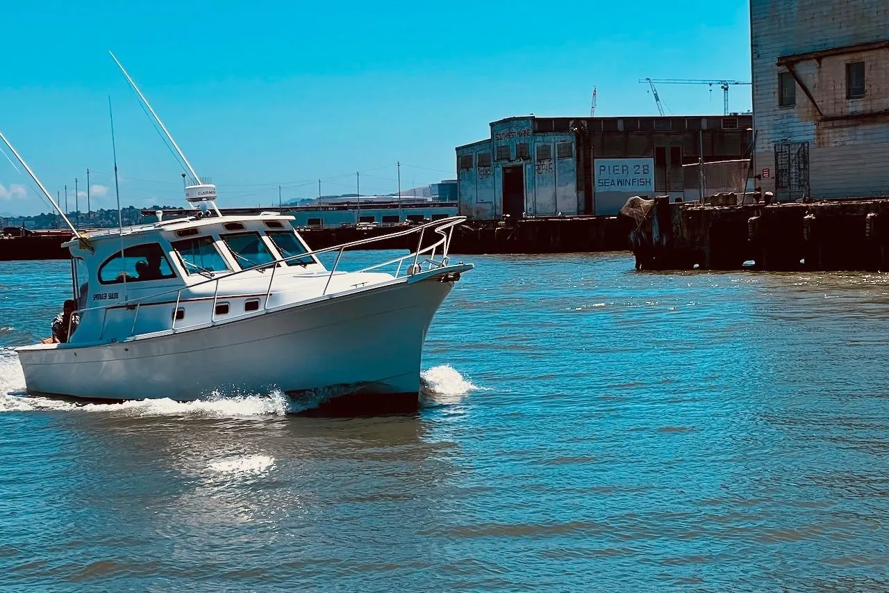 1999 Mainship Pilot 30 cruising near industrial waterfront, clear blue sky.