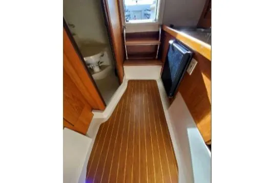 1999 Mainship Pilot 30 interior with wood flooring, compact kitchen, and storage shelves.