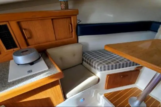 1999 Mainship Pilot 30 cabin interior with seating, table, and wooden cabinetry.