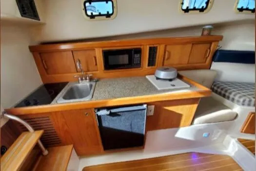 1999 Mainship Pilot 30 interior with kitchenette, featuring wooden cabinetry, sink, microwave, and seating area.