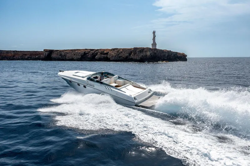 White Chocolate Yacht Photos Pics Speedboat Magnum 44 (2003) cruising near rocky coastline with lighthouse in background.