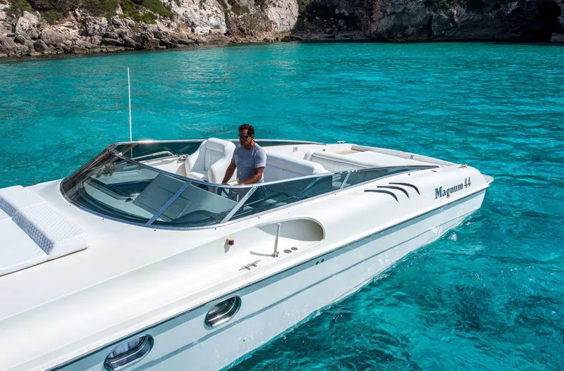 White Chocolate Yacht Photos Pics White Magnum 44 boat from 2003 on clear turquoise water, with rocky shoreline in background.