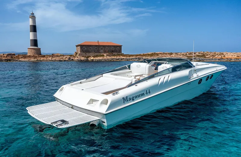 White Chocolate Yacht Photos Pics 2003 Magnum 44 boat near lighthouse and building on clear blue water.