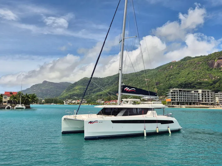 Takamaka Yacht Photos Pics Sailing catamaran Leopard 50 in turquoise waters, lush green hills in the background.