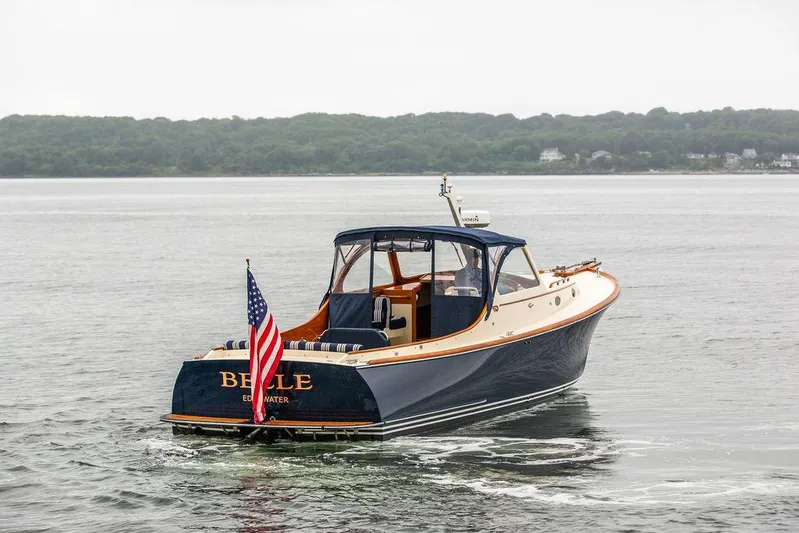 Belle Yacht Photos Pics 1998 Hinckley Picnic Boat on water, displaying American flag, with lush shoreline in background.