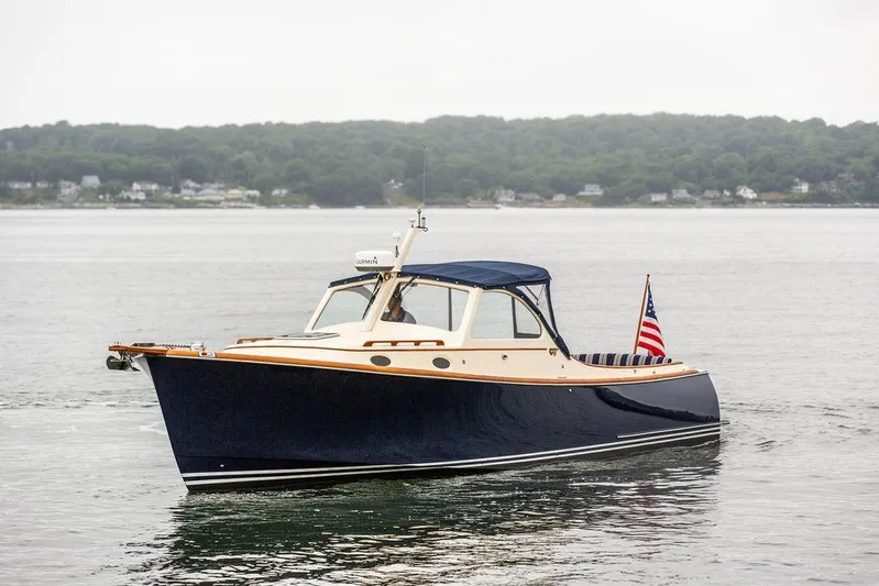 Belle Yacht Photos Pics 1998 Hinckley Picnic Boat on calm water with American flag, scenic shoreline background.