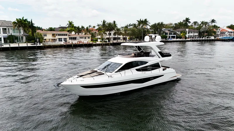 Bugsy Yacht Photos Pics 2020 Galeon 550 Fly yacht cruising on a scenic waterfront with luxury homes in the background.
