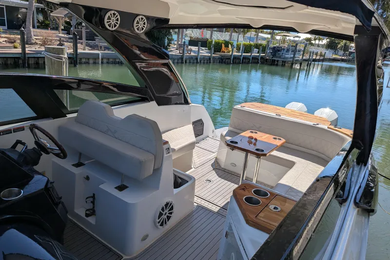 Mbvip Yacht Photos Pics 2023 NX Boats 340 Sport Coupe interior with seating and table, docked by the water.