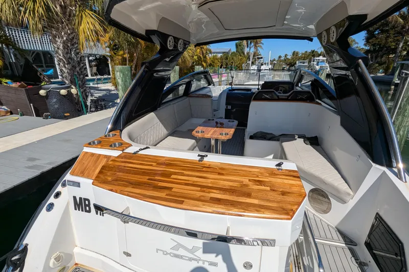 Mbvip Yacht Photos Pics 2023 NX Boats 340 Sport Coupe with sleek interior and wooden accents docked by palm trees.