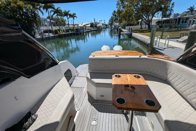 Mbvip Yacht Photos Pics 2023 NX Boats 340 Sport Coupe interior with seating and table, docked by a scenic canal.