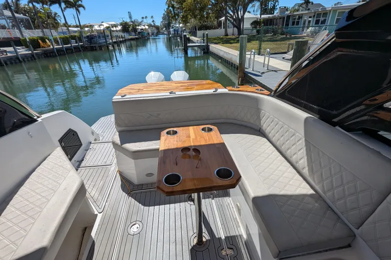 Mbvip Yacht Photos Pics 2023 NX Boats 340 Sport Coupe interior with elegant seating and wooden table by the water.