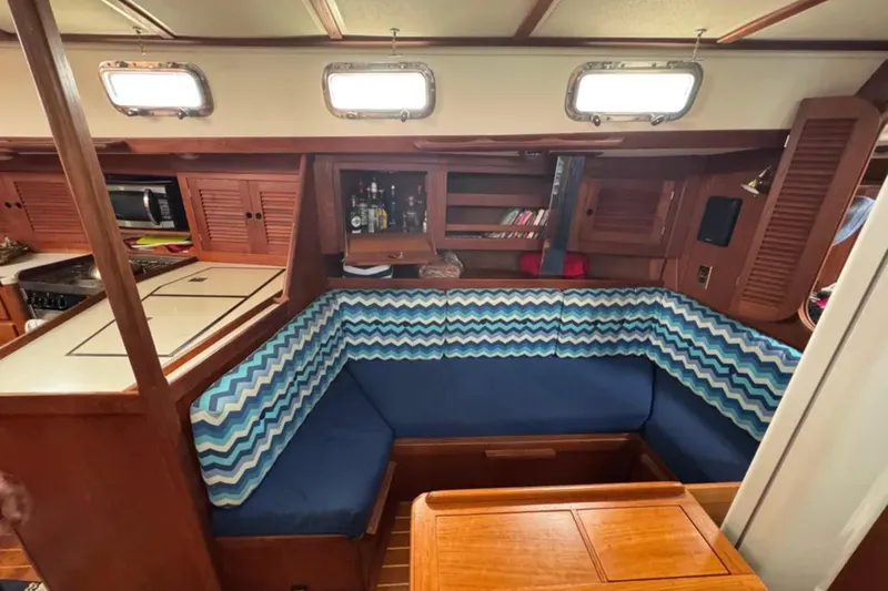 Bittersweet Yacht Photos Pics 1989 Tartan 4100 yacht interior with blue chevron seating, wooden cabinetry, and kitchenette.
