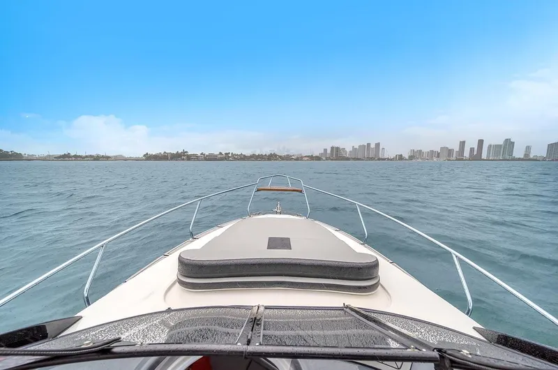  Yacht Photos Pics Bow view of 2024 Hanover 305 boat cruising towards city skyline under clear blue sky.