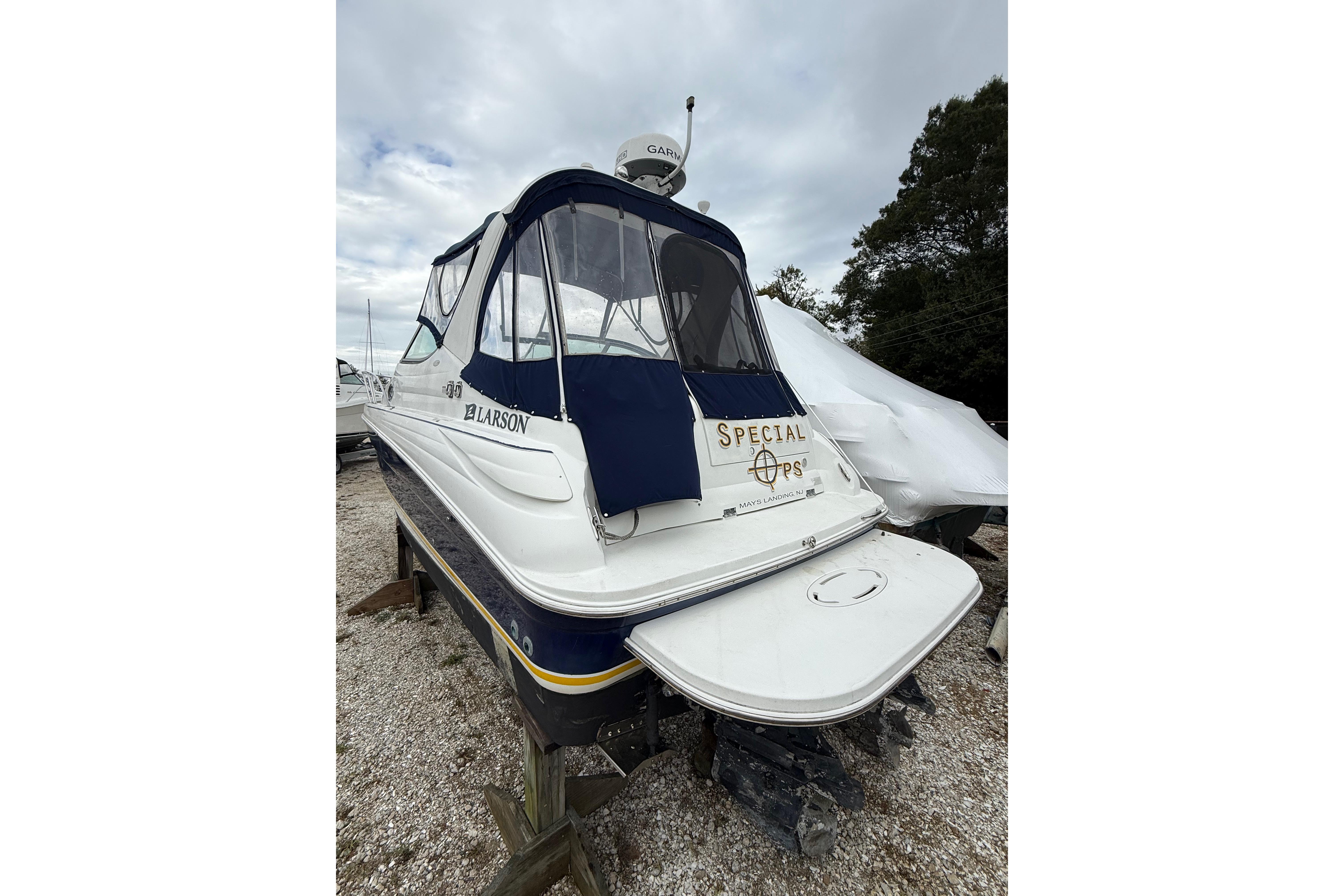 2005 Larson Cabrio 290 boat with blue canopy, parked on gravel.