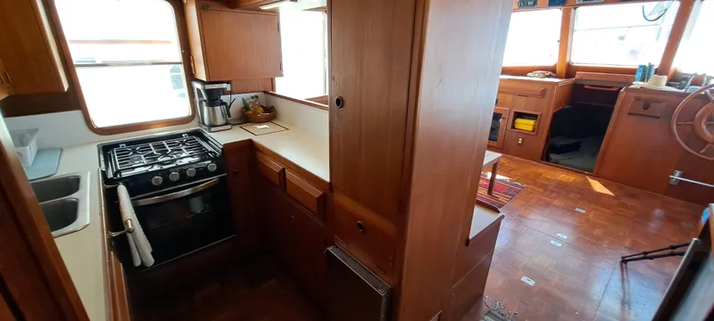 Ballena Blanca Yacht Photos Pics 1985 DeFever 44 Trawler interior with kitchen and helm, featuring wood cabinetry and flooring.