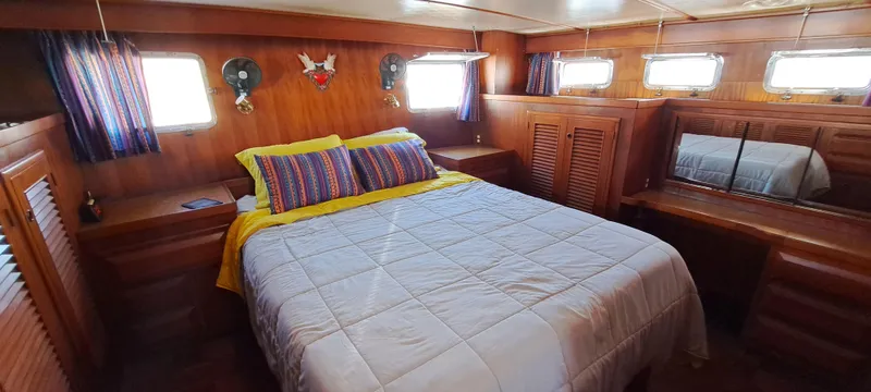 Ballena Blanca Yacht Photos Pics Cozy bedroom interior of 1985 DeFever 44 Trawler with wood paneling and colorful bedding.