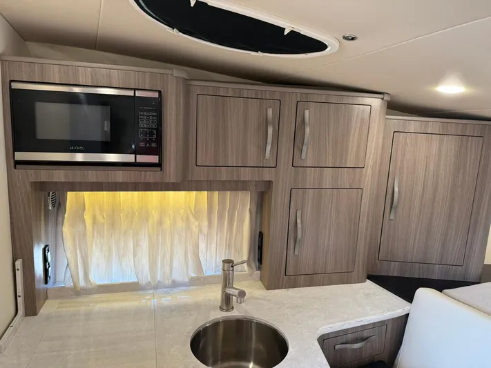  Yacht Photos Pics 2021 Regal 33 XO boat interior kitchen with microwave, sink, and wooden cabinets.