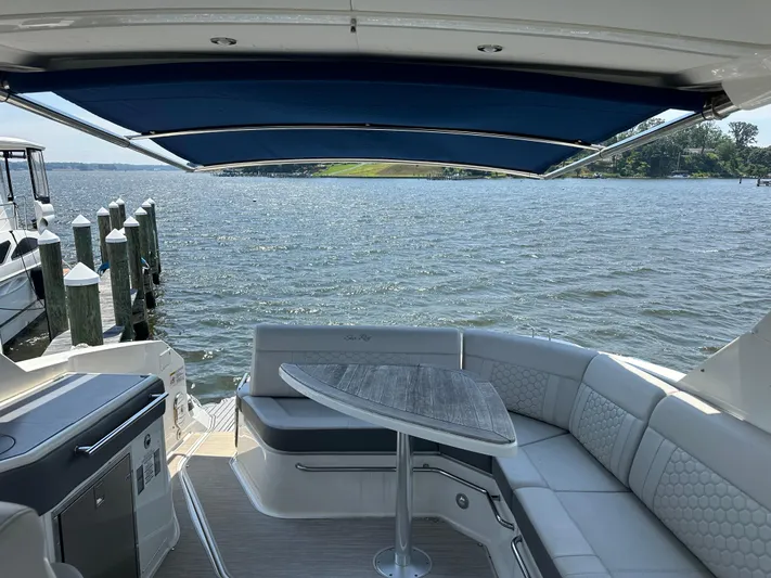  Yacht Photos Pics 2021 Sea Ray 320 Sundancer boat interior with seating and table, overlooking a scenic waterfront.