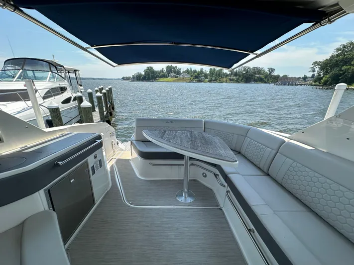  Yacht Photos Pics 2021 Sea Ray 320 Sundancer boat interior with seating and table, docked by the water.