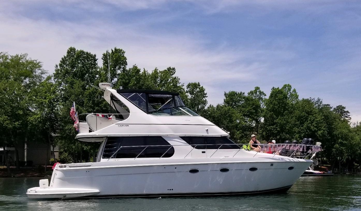 2001 Carver 450 Voyager Pilothouse yacht on a serene lake with lush trees.