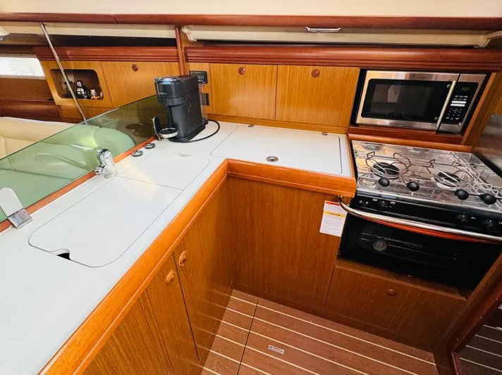 La Dauphine Yacht Photos Pics 2007 Jeanneau Sun Odyssey 36i yacht kitchen with stove, microwave, and wooden cabinetry.