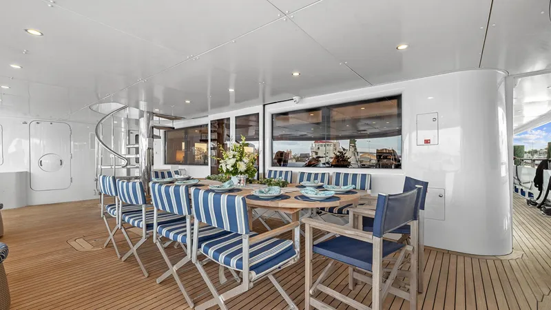 My Spirit Yacht Photos Pics Outdoor dining area on 2005 New Zealand Yachts Wave Piercer, featuring striped chairs and wooden table.