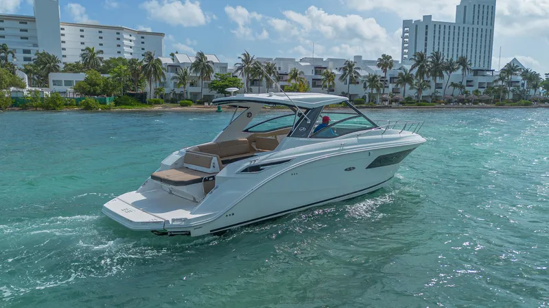 White Kraken Yacht Photos Pics 2023 Sea Ray Sundancer 320 cruising in clear blue waters near a coastal city.