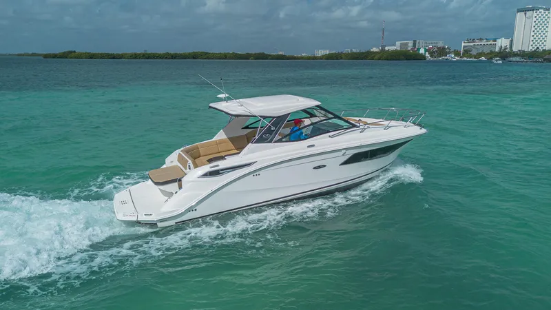 White Kraken Yacht Photos Pics 2023 Sea Ray Sundancer 320 cruising on turquoise waters under a cloudy sky.