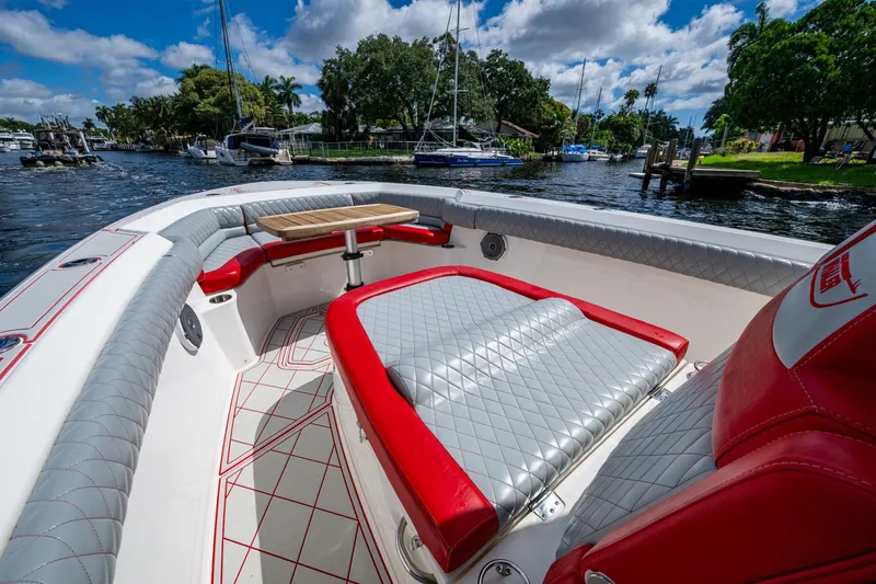 Dare To Dream's Sidechick Yacht Photos Pics 2018 Boston Whaler 330 boat interior with red and gray seating, docked by a scenic waterfront.