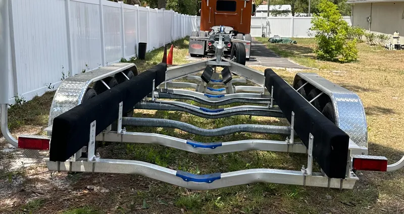  Yacht Photos Pics Boat trailer for 2018 Sailfish 325 DC, parked on grass near a white fence.