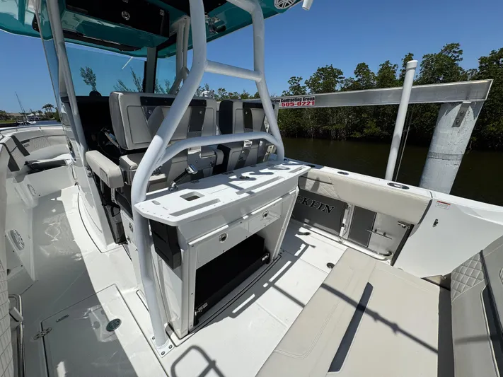  Yacht Photos Pics 2021 Blackfin 272 CC boat interior with seating and console, docked near lush greenery.