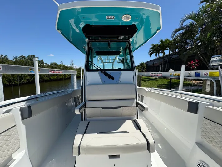  Yacht Photos Pics 2021 Blackfin 272 CC boat interior with seating and console, docked near lush greenery.