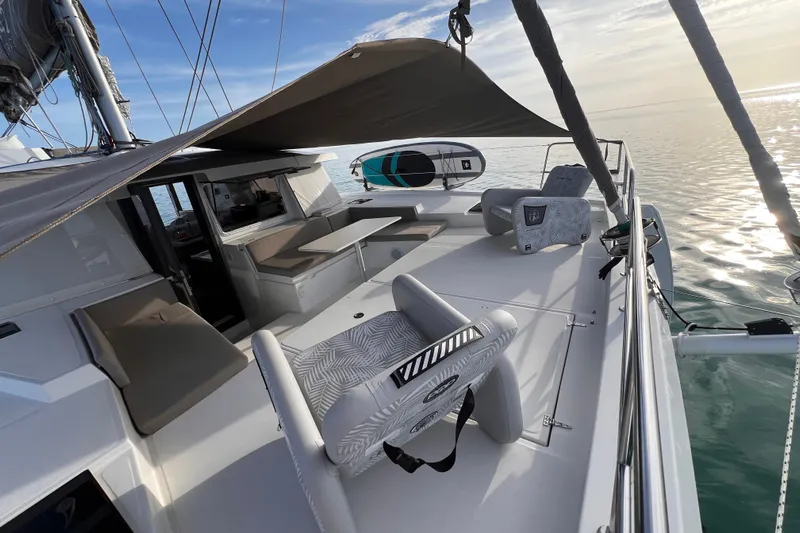 Tamboo Yacht Photos Pics Modern 2023 Bali 4.2 catamaran deck with seating, sunshade, and paddleboard on calm sea.