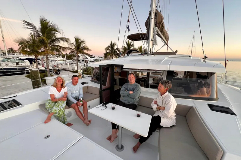 Tamboo Yacht Photos Pics Group relaxing on a 2023 Bali 4.2 catamaran at sunset, docked near palm trees.