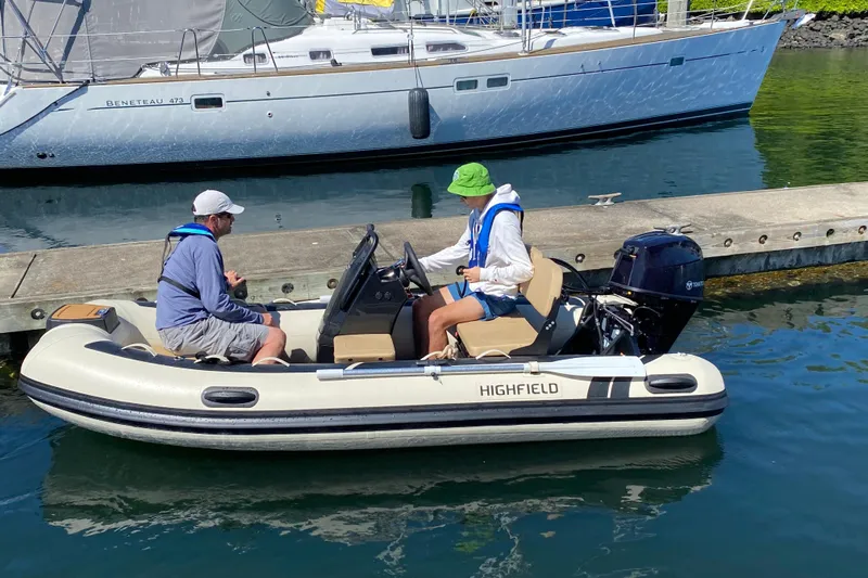  Yacht Photos Pics Two people in a small motorboat near a dock, with a larger boat in the background.
