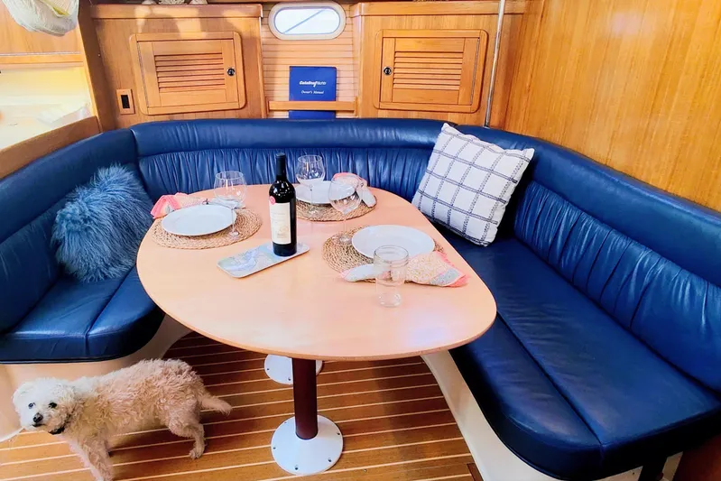 Alola Yacht Photos Pics Cozy dining area in 2003 Catalina 42 MkII yacht with blue seating and a small dog.