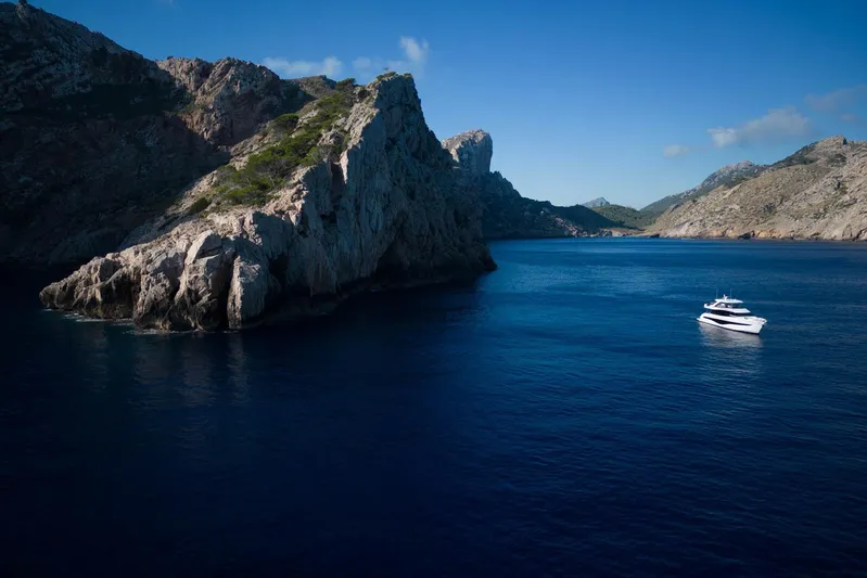  Yacht Photos Pics Luxurious 2024 Princess Y80 yacht cruising near rocky coastline under clear blue sky.