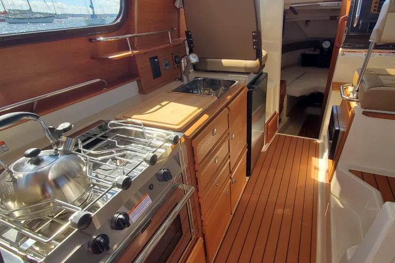 Tusen Takk Yacht Photos Pics 2024 Ranger Tugs R-27 interior with kitchenette, featuring stove, sink, and wooden cabinetry.
