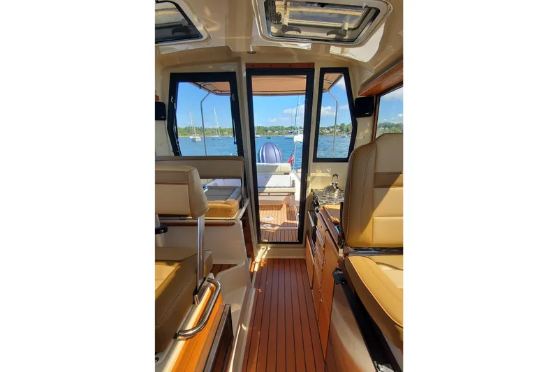 Tusen Takk Yacht Photos Pics 2024 Ranger Tugs R-27 interior with tan seating, wood flooring, and scenic water view.