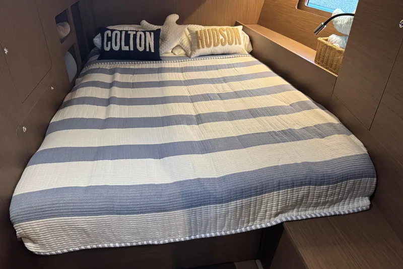  Yacht Photos Pics Cozy cabin interior of 2023 Beneteau Oceanis 46.1 with striped bedding and decorative pillows.