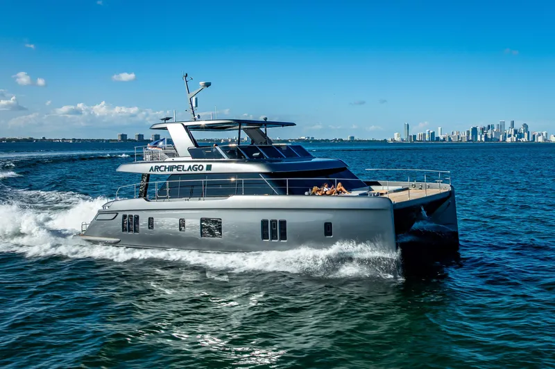 Skip The Wait Yacht Photos Pics 2026 Sunreef 60 Power yacht cruising near city skyline on a sunny day.