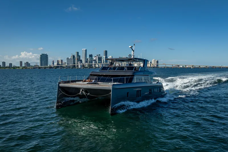 Skip The Wait Yacht Photos Pics 2026 Sunreef 60 Power yacht cruising near city skyline on a sunny day.