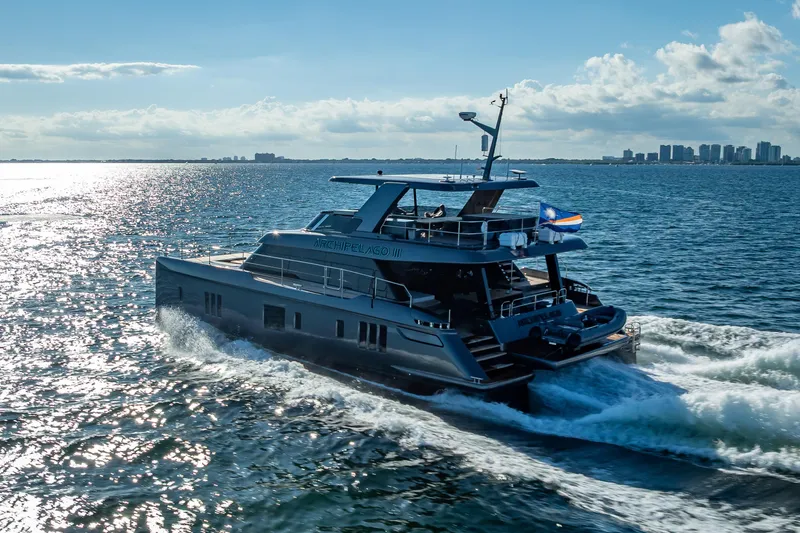 Skip The Wait Yacht Photos Pics Luxurious 2026 Sunreef 60 Power yacht cruising on open water, city skyline in background.