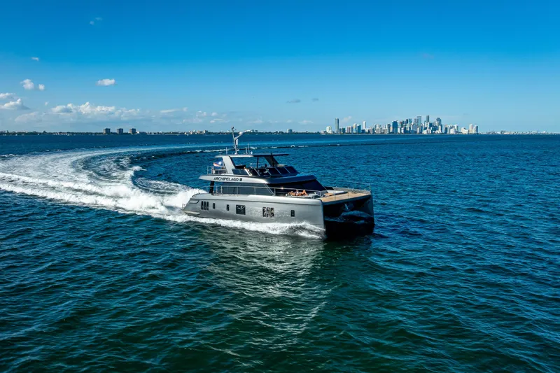 Skip The Wait Yacht Photos Pics 2026 Sunreef 60 Power yacht cruising near city skyline on a sunny day.