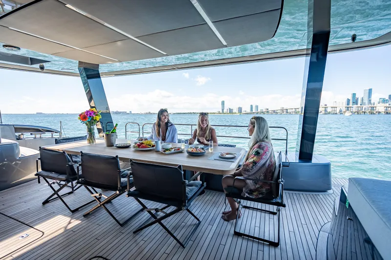 Skip The Wait Yacht Photos Pics Three people dining on a luxurious 2026 Sunreef 60 Power yacht with city skyline views.