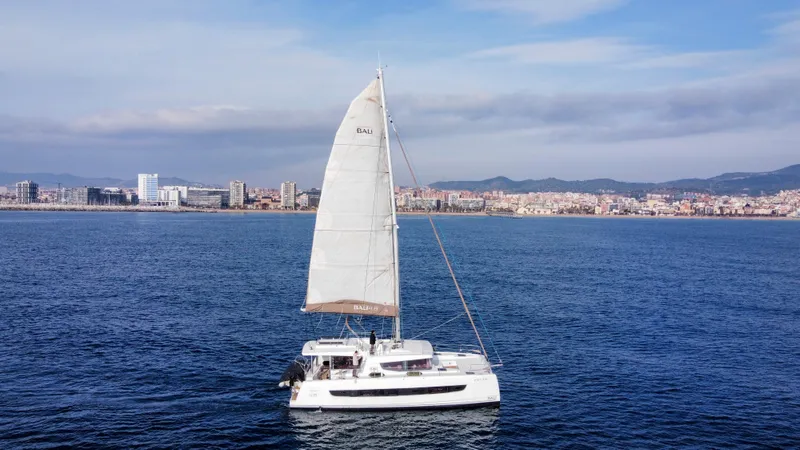 Tatani Yacht Photos Pics 2021 Bali 4.8 catamaran sailing near a coastal city under a clear blue sky.